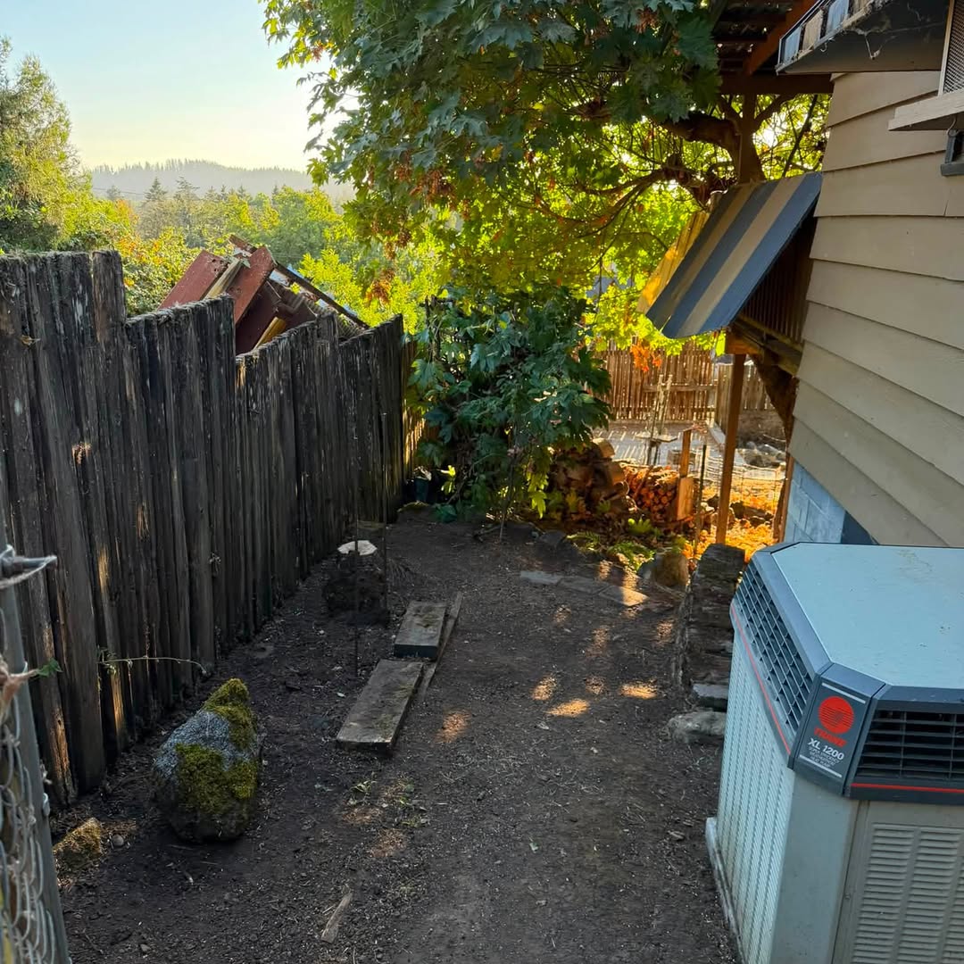 Side yard after clearing, bare earth along the fence and house